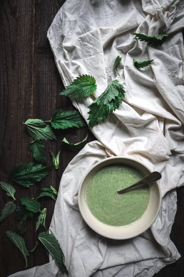 碗绿色的荨麻汤在餐桌装饰用布和宽松的荨麻叶子