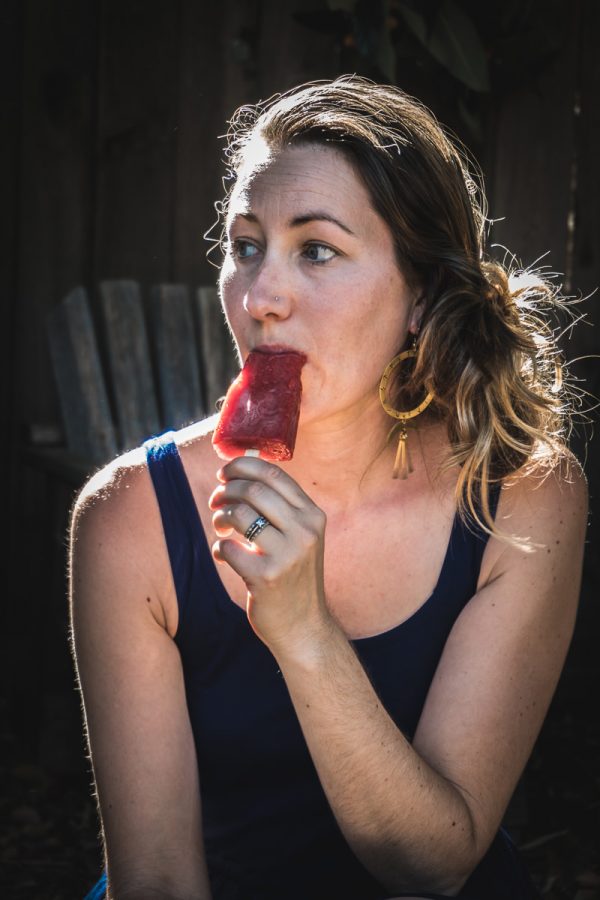 一个穿蓝色裙子的女人坐在外面吃草莓冰棍。